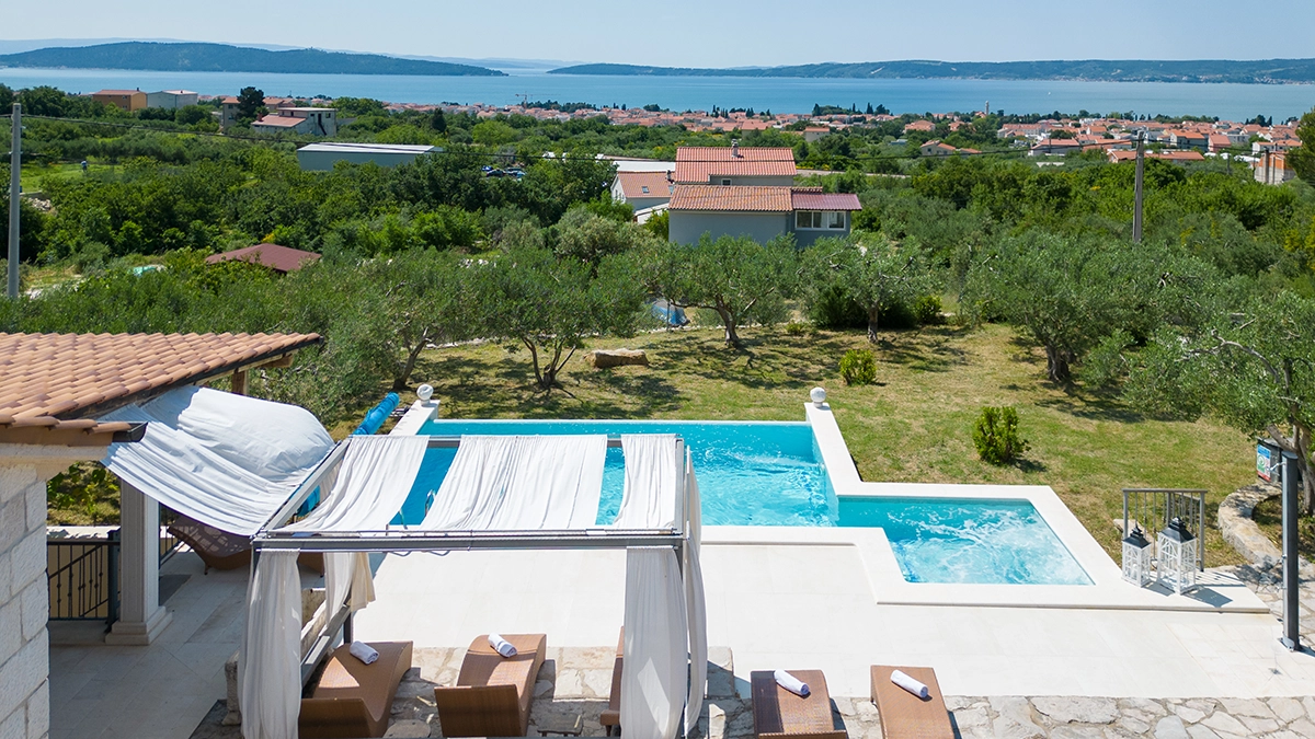 Half-bird's-eye view of the villa's pool and garden with olive trees, overlooking the Adriatic Sea and nearby islands.